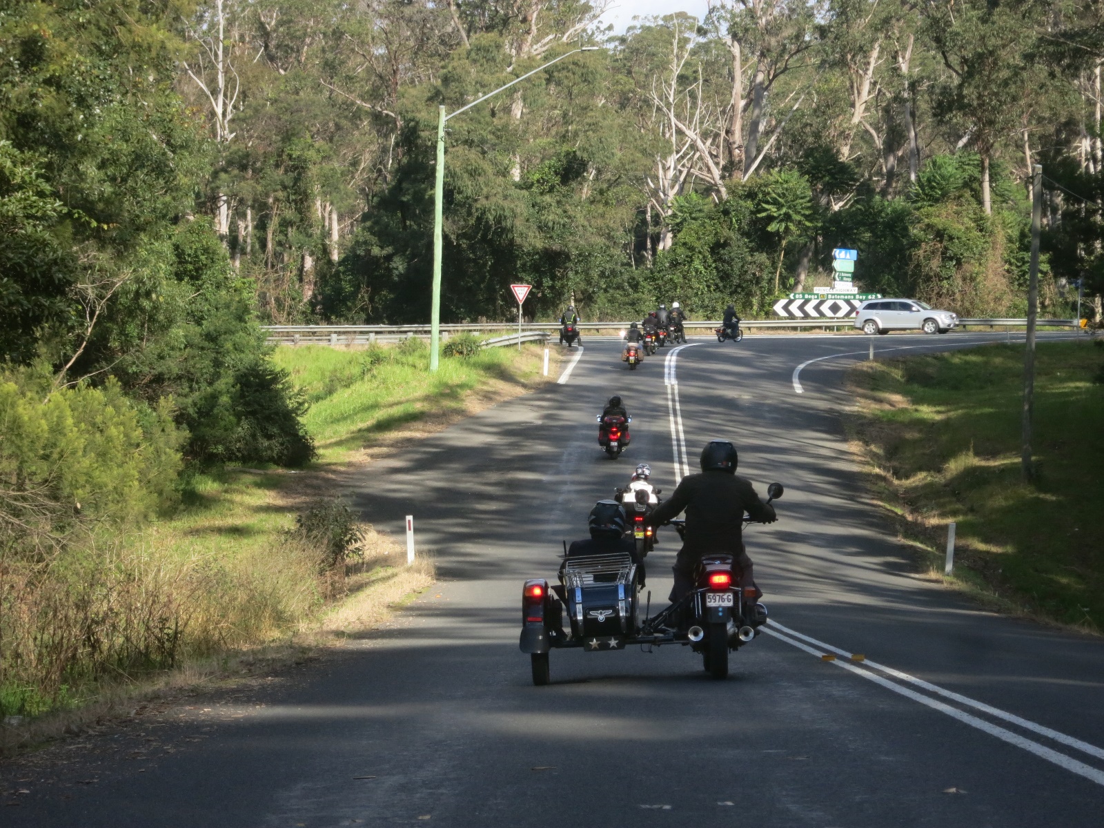 A group of people ride motorcycles down a road Description automatically generated with medium confidence