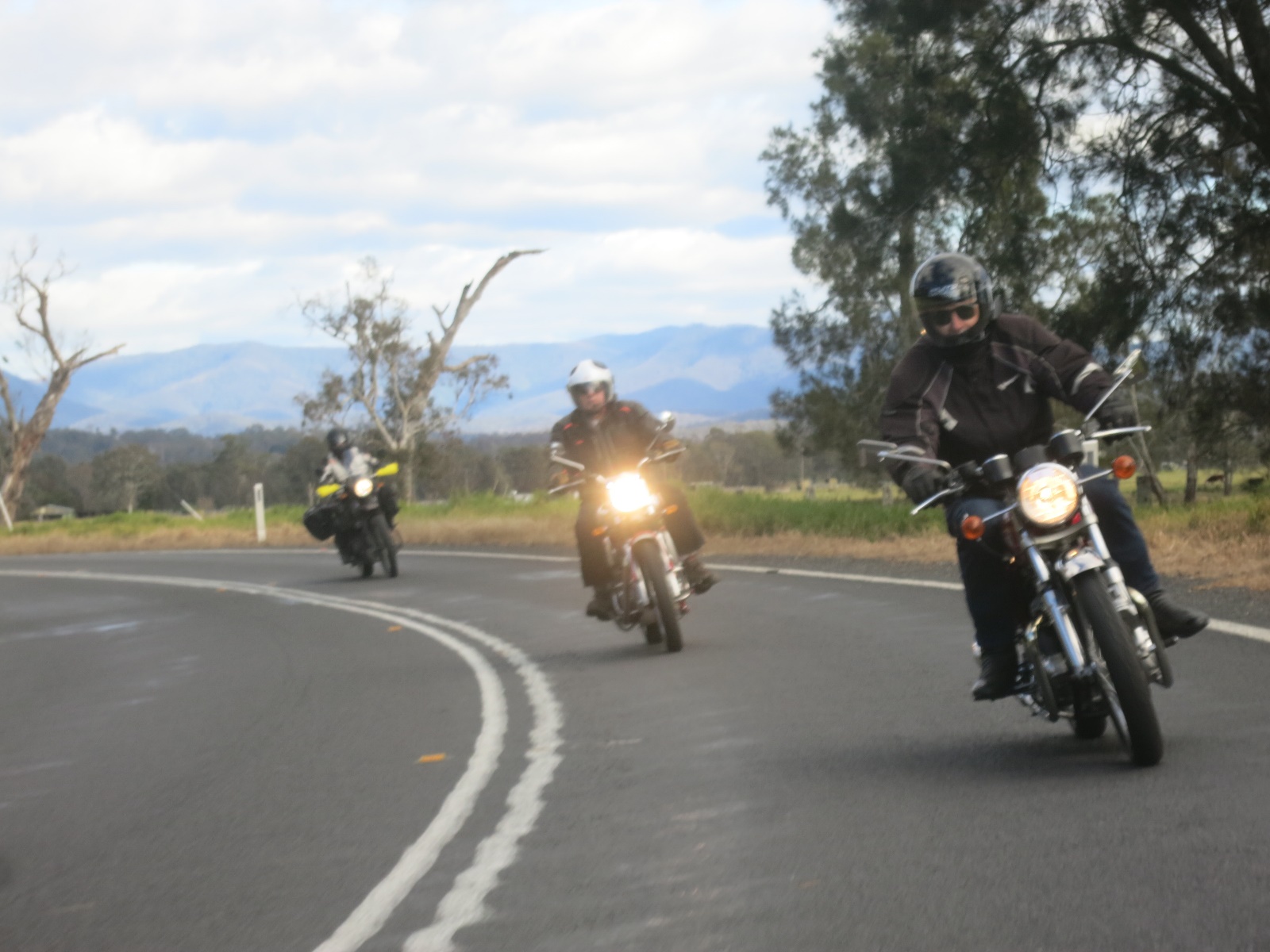 A group of people ride motorcycles down a road Description automatically generated with medium confidence