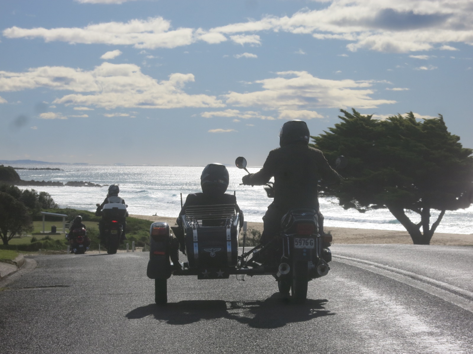 A group of people ride motorcycles down a road Description automatically generated with low confidence
